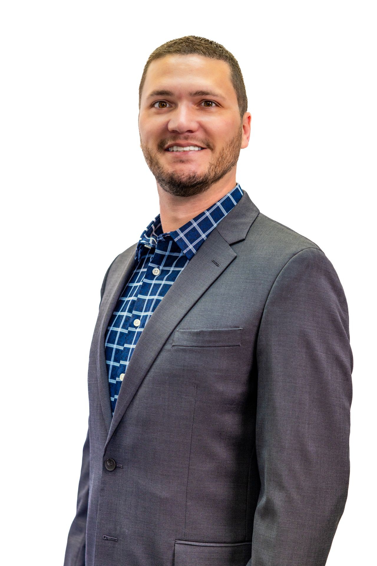 Man in a dark grey suit jacket and blue plaid shirt standing against a white background.