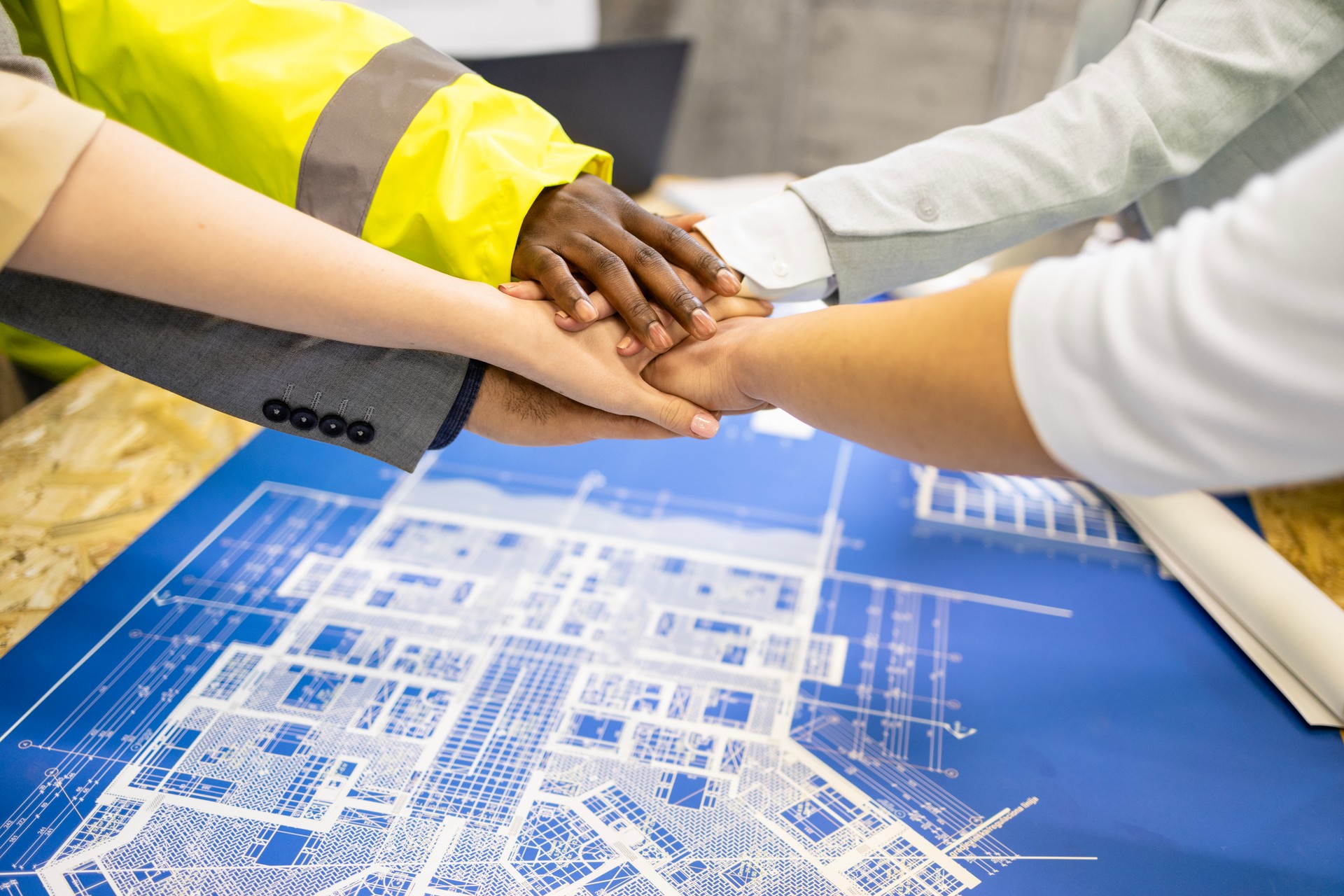 Holding hands together above building plans and blueprints at construction site. Architects and structural engineers.